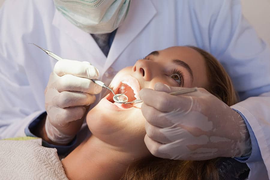 Dentist examining a female patient's teeth with a dental mirror.
