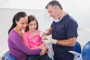 Pediatric dentist using a teeth model to explain oral hygiene to a mother and daughter.