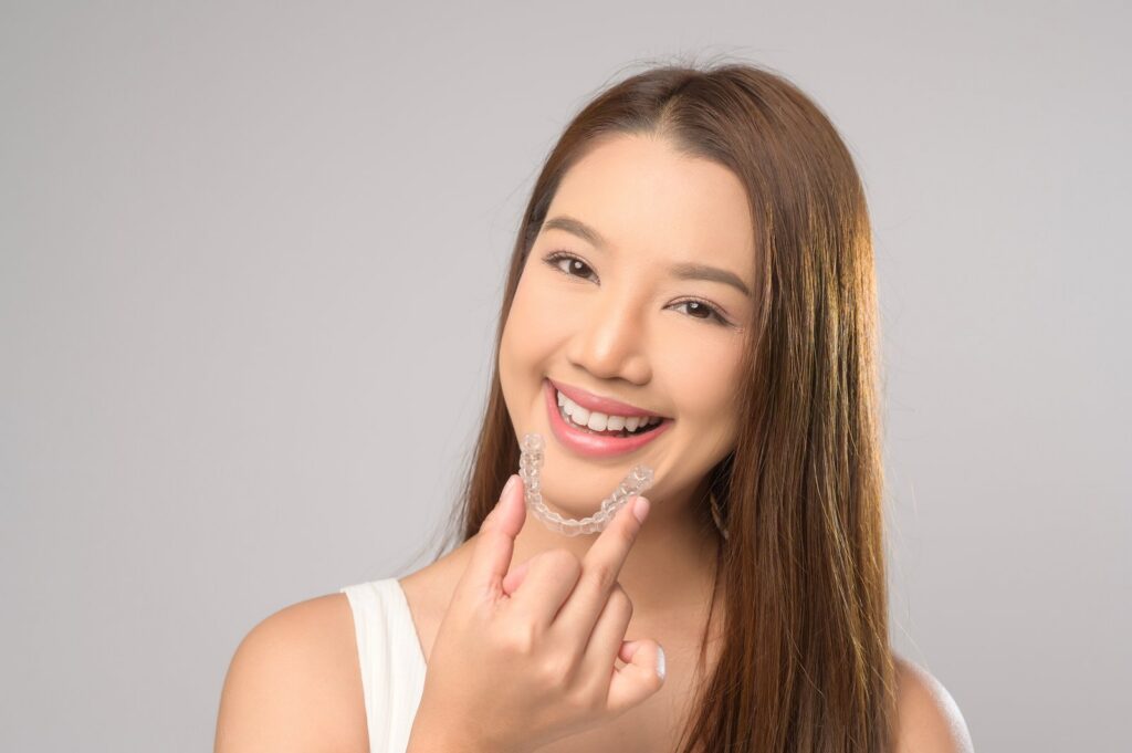 Smiling woman holding clear dental aligners
