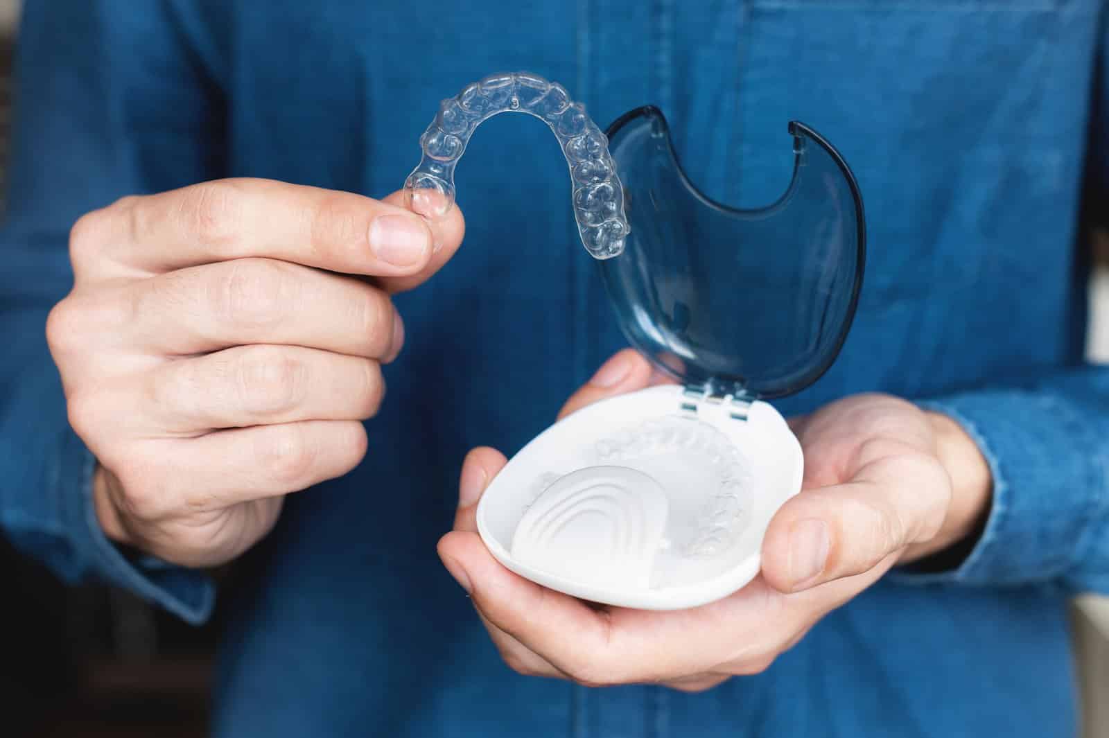 Close-up Of A Young Caucasian Man Holding An Invisible Dental Retainer And A Case For Their Storage